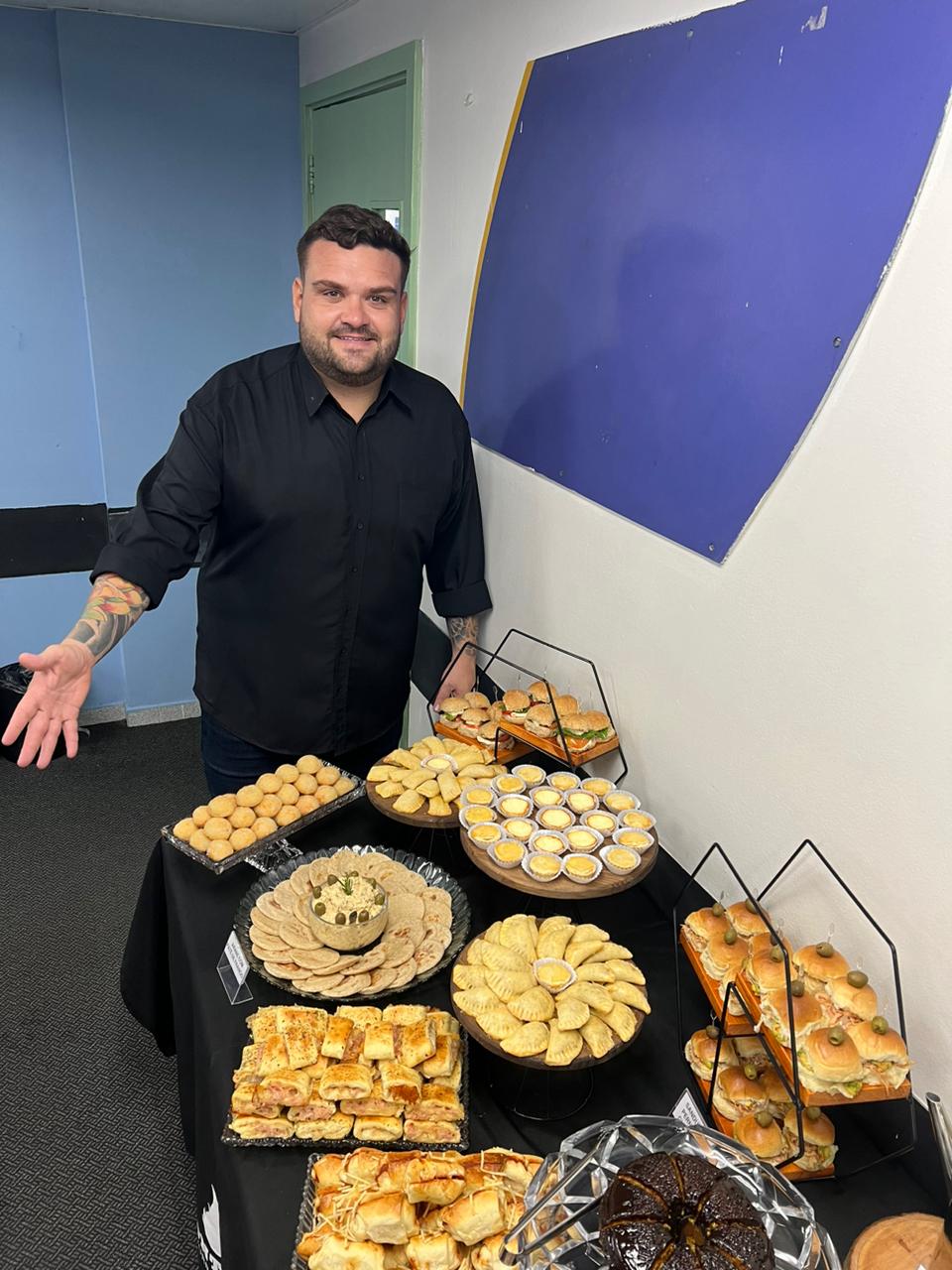 Mesa de buffet com lanches e salgados e Monteiro ao lado